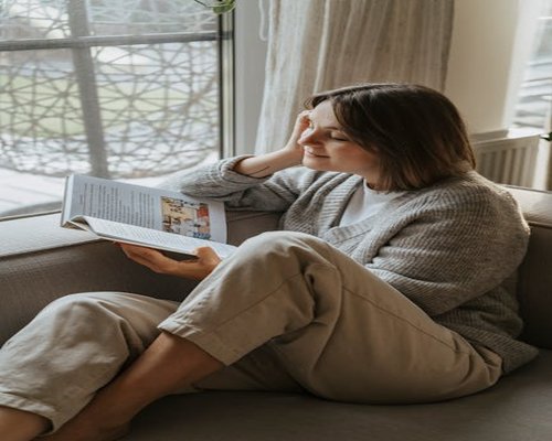 Persona relajada leyendo un libro en un sofá cómodo cerca de una ventana
